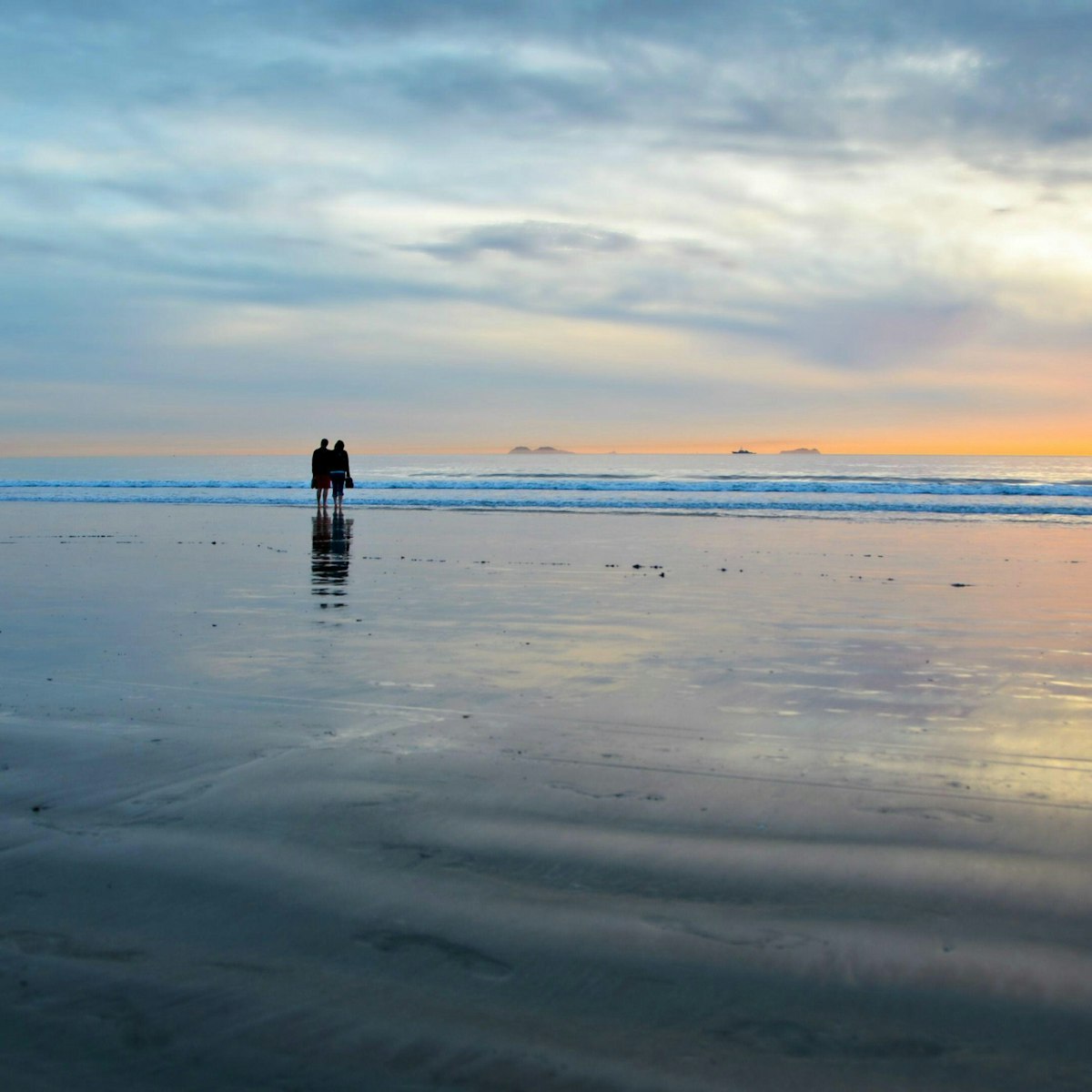 2E5BKXB Young couple silhouettes on the Silver Strand Beach wet sand watching the sunset at Coronado Island, San Diego Southern California USA.